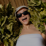 Woman relaxing in the sauna with a bath broom and wearing a sauna hat